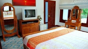 Habitación de hotel con una cama, televisor, cómoda de madera, espejo y puerta.