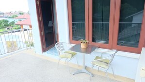 Un balcón con dos sillas, una mesa, una planta en maceta y vistas a edificios cercanos.