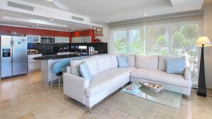 Een moderne keuken met een centraal eiland, een witte bank en een groot raam met uitzicht op groen.