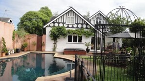 Une maison avec une piscine, un jardin clos et une terrasse aménagée avec du mobilier d’extérieur.