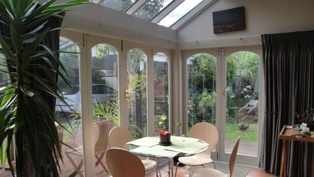 Une véranda avec un toit en verre, une table à manger avec des chaises et une plante en pot.