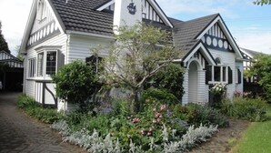 Une maison traditionnelle avec un toit à forte pente, une cheminée et un jardin agrémenté de plantes à fleurs et d’un sentier.
