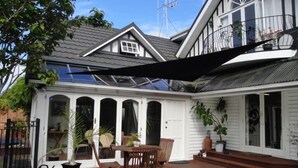 Une maison dotée d’un patio couvert, d’un coin repas avec des chaises et une table, et d’un balcon agrémenté de plantes en pot.