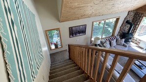 Una escalera de madera con barandilla que lleva a una sala de estar con chimenea y vistas al exterior.