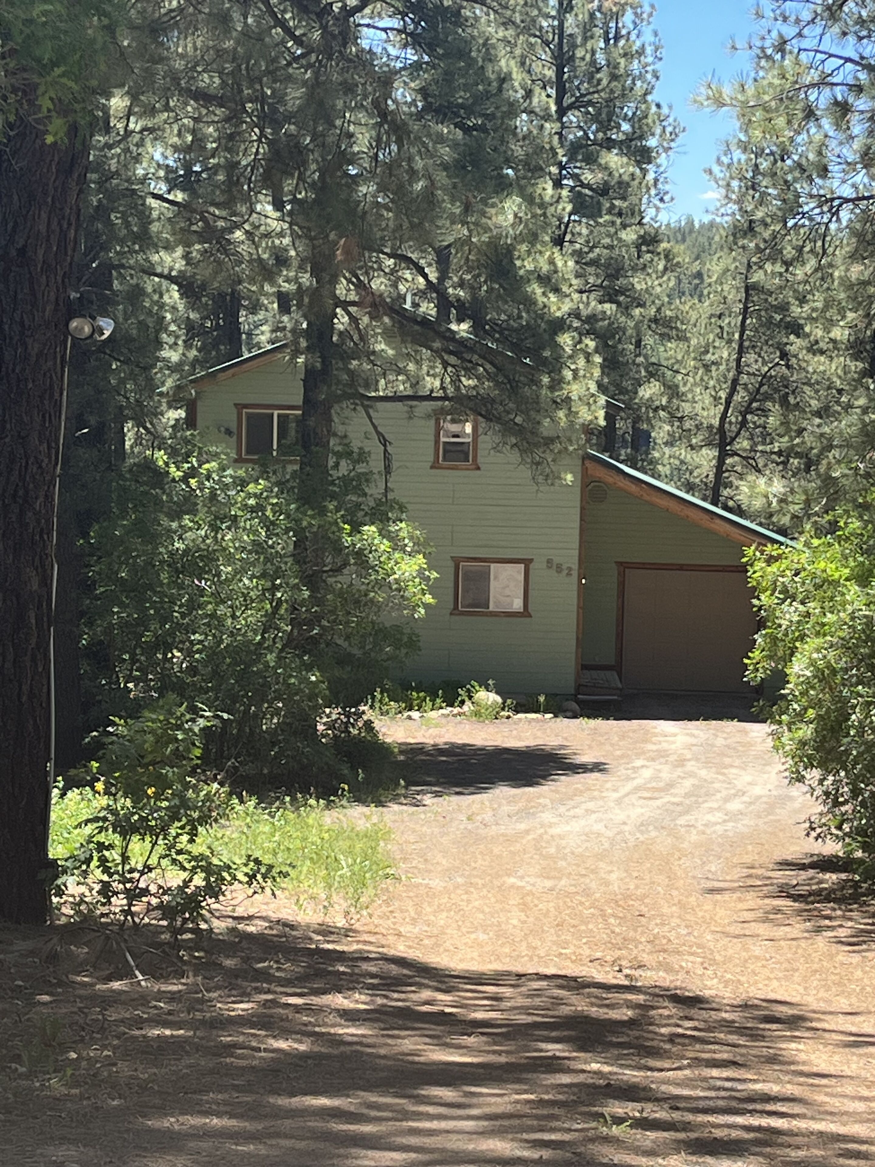 A two-story house with a garage, surrounded by dense trees and a dirt driveway.