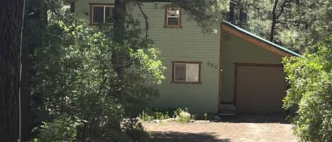 A two-story house with a garage, surrounded by dense trees and a dirt driveway.