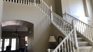 A multi-level interior with a white staircase, a ceiling fan, and a lamp on the landing.