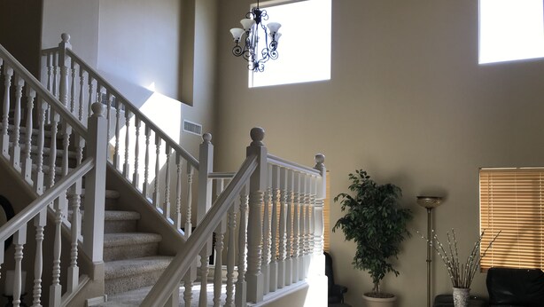 A spacious living area with a staircase, a potted plant, a floor lamp, and a window with blinds.