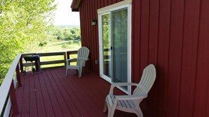 A red wooden deck with two white chairs and a barbecue grill.