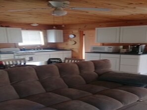 Een gezellig cabin interieur met een modulaire bank, houten plafond, witte kasten en een kitchenette.
