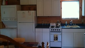 A compact kitchen with white cabinets, a stove, a sink, and a window providing natural light.