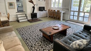 Amplia sala de estar con chimenea, zona de comedor con sillas de madera y ventanas grandes que dejan entrar luz natural.