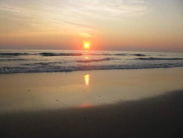 A beach at sunset with waves approaching the shore.