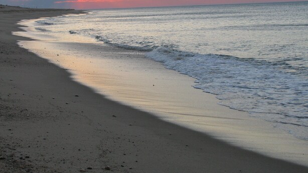 Una playa con olas suaves y un cielo al atardecer.