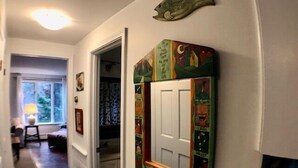 Ein Flur mit einer Fischdekoration über einer Tür, einem Fenster mit Blick auf Bäume und einer Tür mit farbenfroher Kunst.