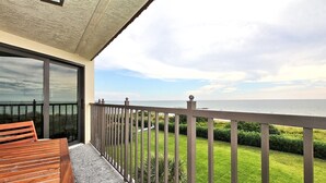 Een balkon met een houten bankje, uitzicht op zee en een verzorgd gazon.