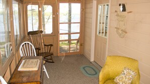 L’intérieur d’un chalet accueillant, avec une porte en bois, une table sur laquelle est posé un menu, un fauteuil jaune et une fenêtre donnant sur un paysage naturel.