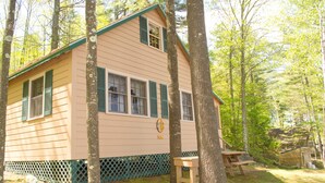 Une petite cabane à un seul étage, dotée d’un toit vert et de volets, entourée d’arbres.