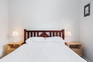Un lit bien fait, avec du linge de lit blanc, une tête de lit en bois et deux tables de chevet avec des lampes.