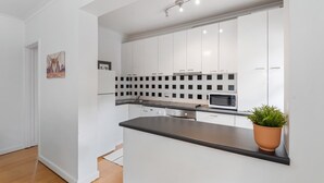 A modern kitchen with white cabinets, a black countertop, and a microwave. - Comfy One-Bedroom Unit Between City and Airport (Travancore)