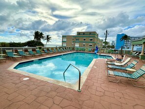 A swimming pool with lounge chairs and a building in the background. - Oceanfront 2 Room Suite with Resort Amenities. (Hollywood)