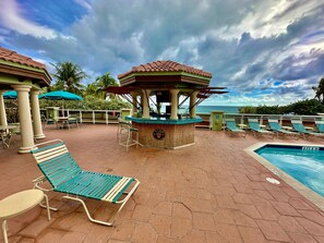 A poolside area with lounge chairs, a bar, and a view of the ocean. - Oceanfront 2 Room Suite with Resort Amenities. (Hollywood)