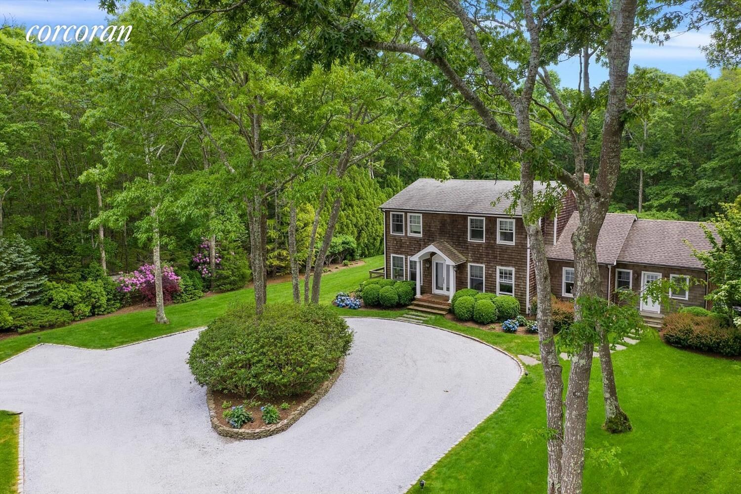 A two-story house with a well-maintained lawn, a driveway, and mature trees.