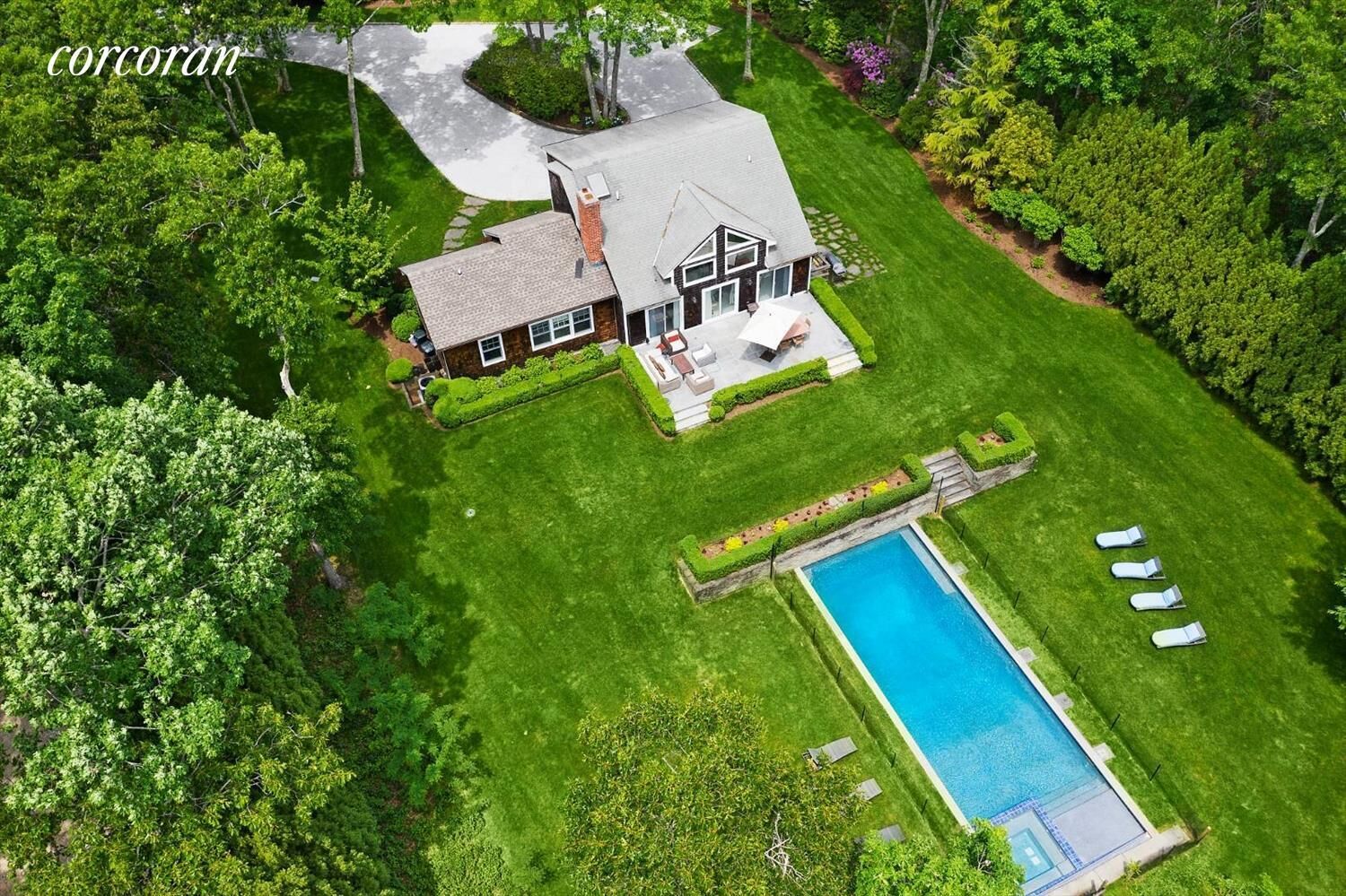 Una vista aerea di una casa con piscina, circondata da prati curati e alberi.