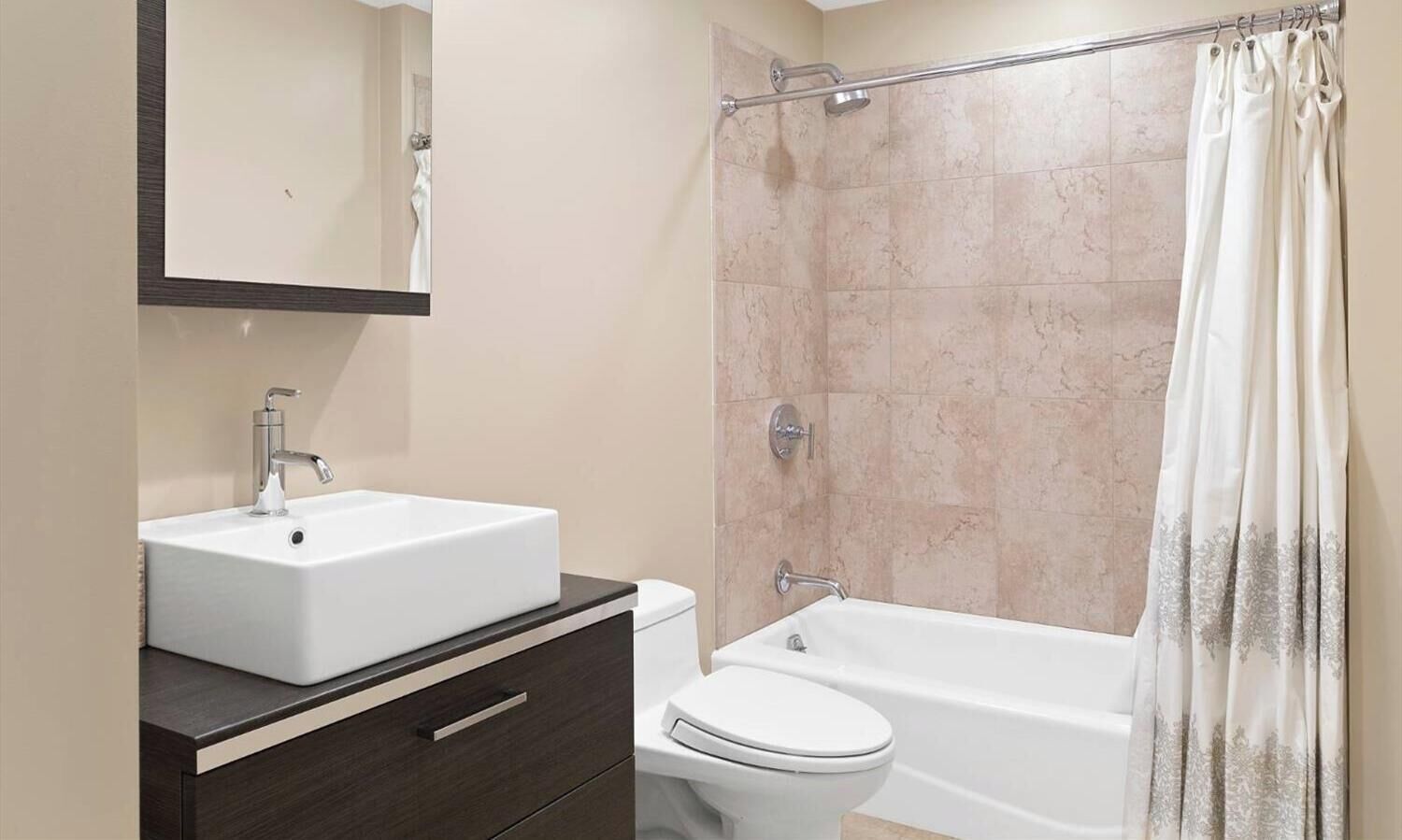 Ein Badezimmer mit weißem Waschbecken, einer Toilette, einer Badewanne, einem dunklen Holzschrank und einer Dusche mit Glastür.