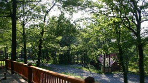 A wooden deck with a railing overlooking a road and a building surrounded by trees.