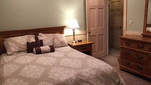 A bedroom with a bed, a nightstand, a dresser, and a door.