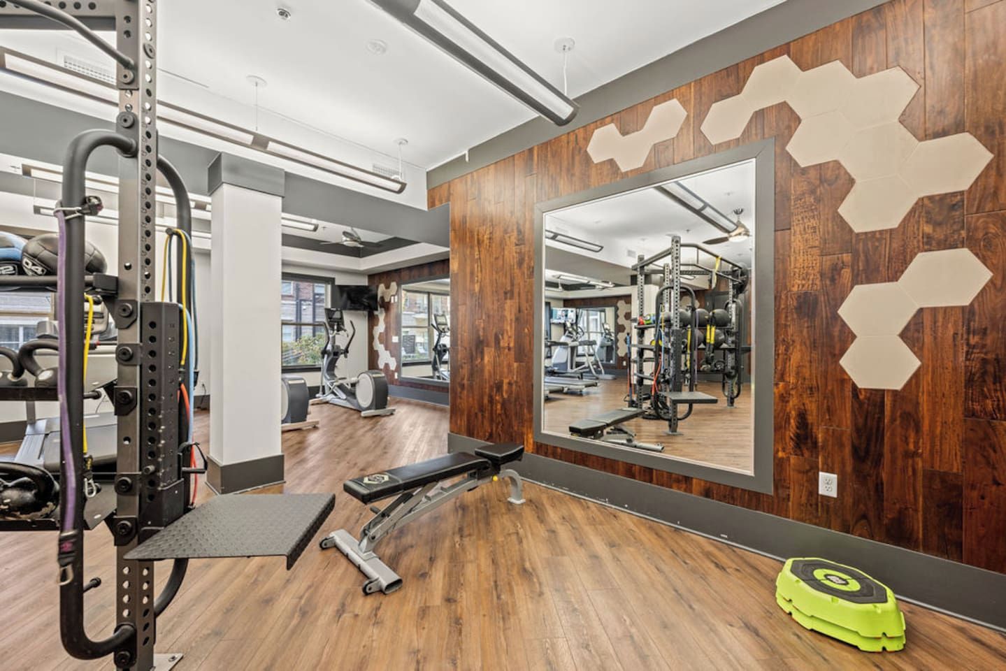 A gym with exercise equipment, a mirror, and wooden flooring.