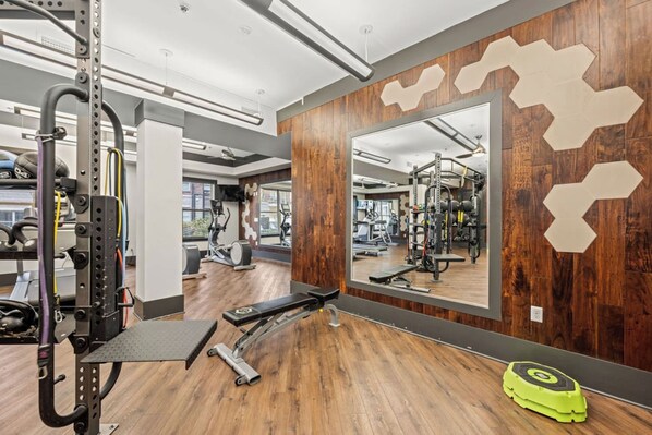 A gym with exercise equipment, a mirror, and wooden flooring.