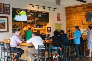 Una zona de bar con decoración de madera, una pizarra con la carta y clientes sentados y de pie.