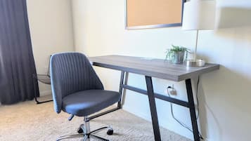 A room with a desk, chair, lamp, and a corkboard on the wall.