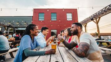 A group of people toasting at a wooden table outdoors with a red building in the background.