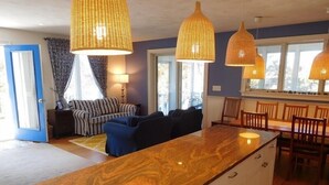 A modern kitchen with a central island, pendant lights, and a dining area with wooden chairs. - Attractive 3BR Cape Home Close to Indian Neck Beach (1430) (Wellfleet)