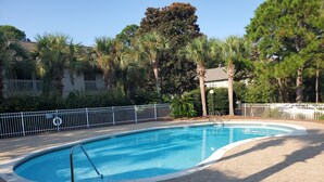 Una piscina con recinzione bianca, circondata da palme e da un patio in mattoni.