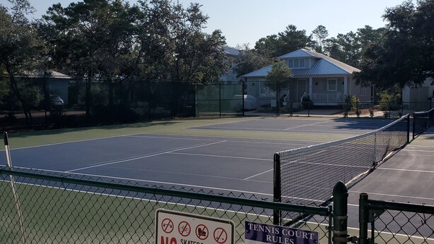 Un campo da tennis recintato con un cartello che vieta pattinaggio su skateboard, biciclette, pattini a rotelle e monopattini.