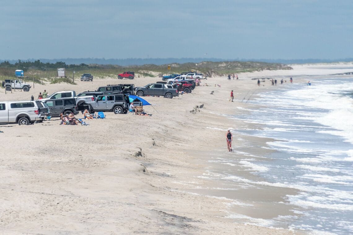 A beach with parked vehicles and people.
