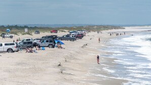 Una playa con vehículos estacionados y gente.
