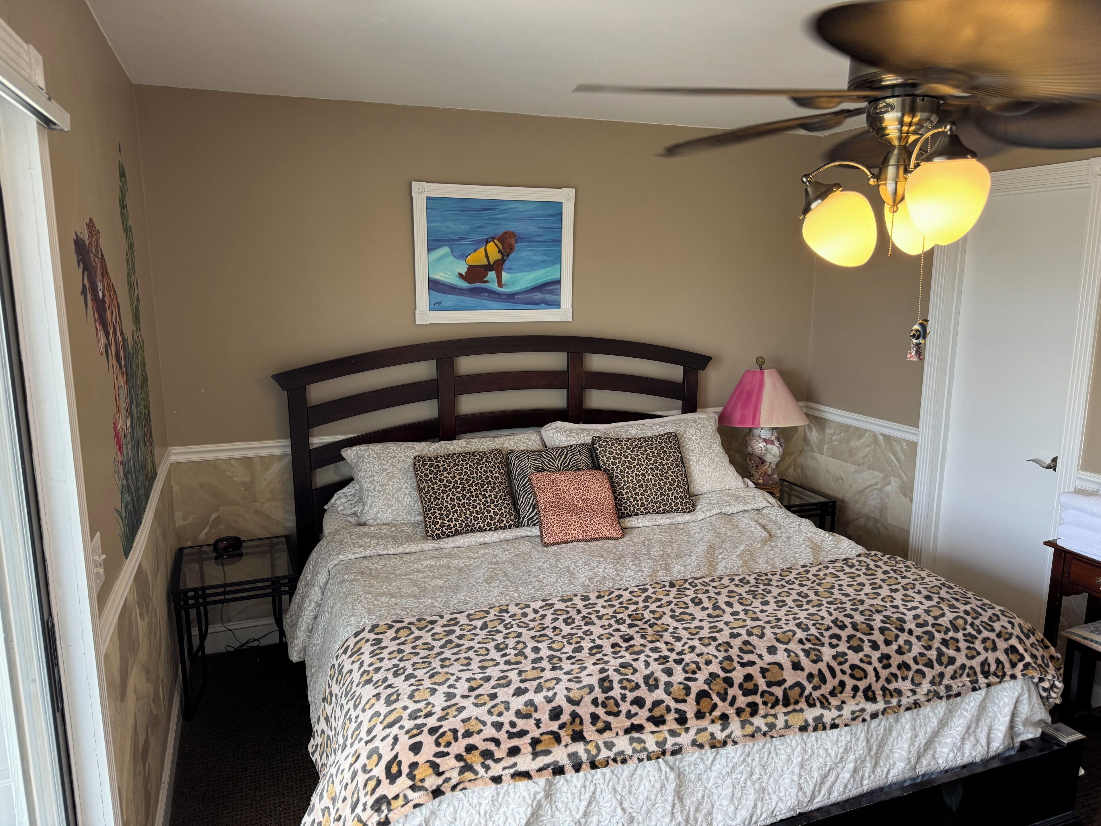 Une chambre à coucher avec un lit, un ventilateur de plafond, un tableau et une lampe.