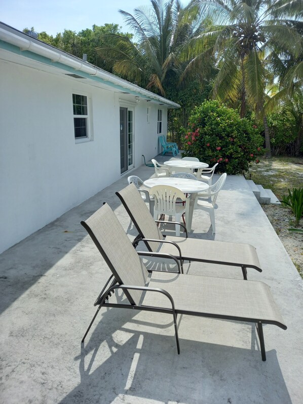 A patio with outdoor furniture, a white building, and surrounding greenery. - Spacious 4 Bedroom 2 Bath Villa, 2 minute walk to beach, Kayak Included (Eleuthera)