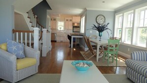 A spacious living room with a white coffee table, a wicker sofa with yellow cushions, a striped armchair, and a dining area with a green chair and a vase of flowers. - Accommodates 12 Guests Overlooking Cape Cod Bay, 6 BR/6 BTH (2048) (Dennis)