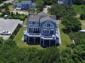 A large, two-story house with a balcony and a covered porch, surrounded by greenery and a parking lot. - Accommodates 12 Guests Overlooking Cape Cod Bay, 6 BR/6 BTH (2048) (Dennis)