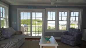 A living room with a sofa, armchair, and a table with a bowl. There are large windows with a view of the sea and a sign above the windows. - Accommodates 12 Guests Overlooking Cape Cod Bay, 6 BR/6 BTH (2048) (Dennis)