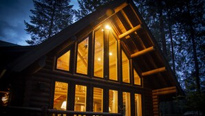 A log cabin with large windows, a porch, and a staircase leading to the entrance. - Beautiful Log Home near Leavenworth, WA. Nestled In The Woods (Peshastin)