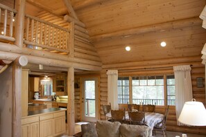 Interior de una cabaña de madera con comedor, cocina y balcón.