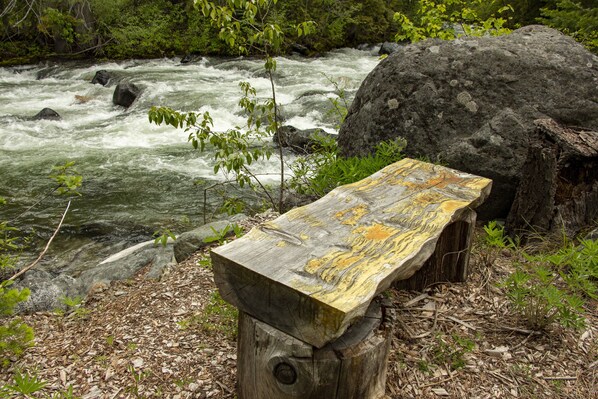 Een houten bank langs een rivier, met een rotsachtige achtergrond en begroeiing.