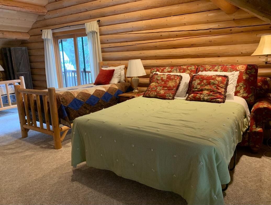 A log cabin bedroom with a bed, a chair, a window, and a lamp.